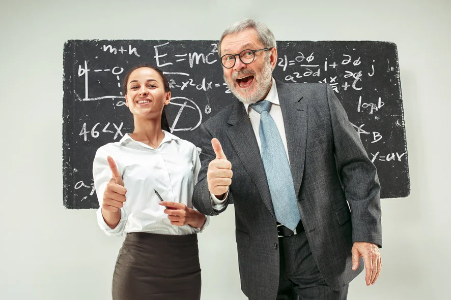 A imagem contém duas pessoas, uma jovem, representando os professores, à esquerda e um senhor de uns 50 anos, representando os educadores, à direita. Ao fundo há uma lousa e os dois estão fazendo joinha com o dedo polegar em riste