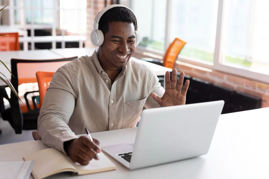 homem aluno de um dentre vários micro cursos, acenando para um laptop, como se estivera em uma aula online