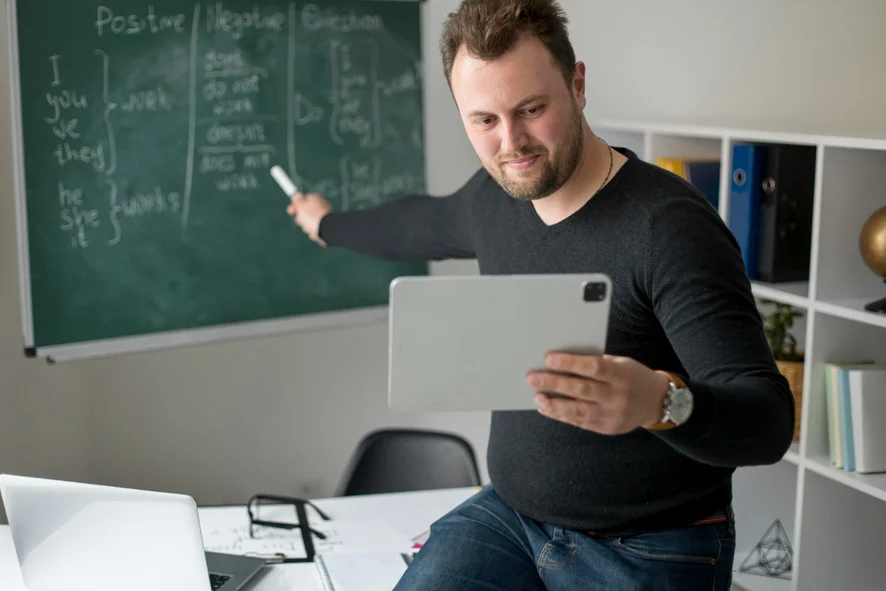 imagem ilustra a presença digital de um professor, com um tablet na mão, transmitindo sua aula pela internet