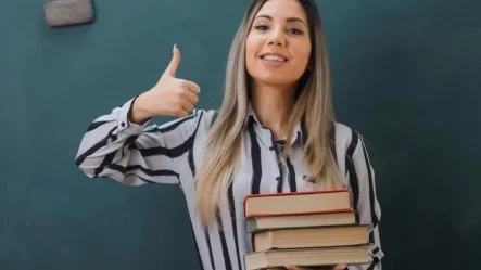 candidata no concurso para professor fazendo um "joinha" com uma mão e um segurando 3 livros na outra, sugerindo uma boa performance