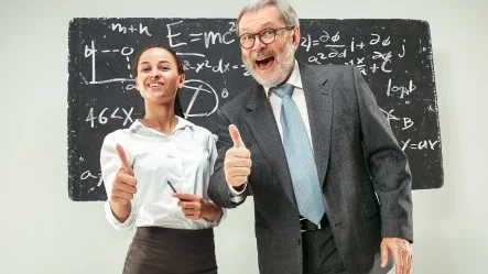 A imagem contém duas pessoas, uma jovem, representando os professores, à esquerda e um senhor de uns 50 anos, representando os educadores, à direita. Ao fundo há uma lousa e os dois estão fazendo joinha com o dedo polegar em riste